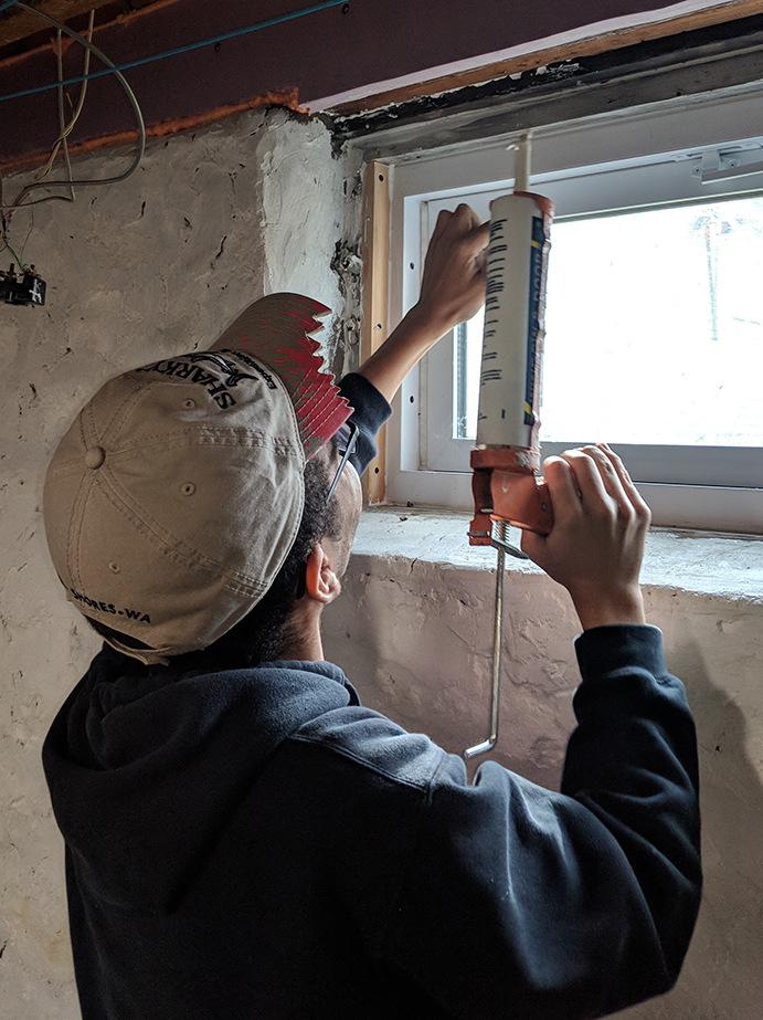 Volunteer caulks window in house