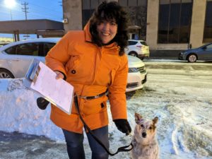 A woman holds a clip board with her dog at her side