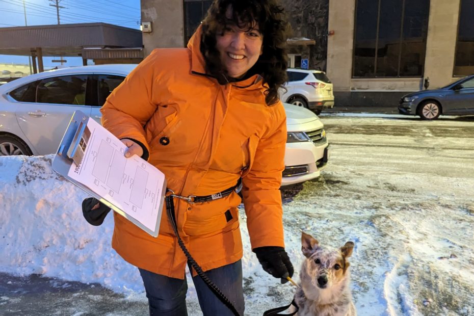 A woman holds a clip board with her dog at her side