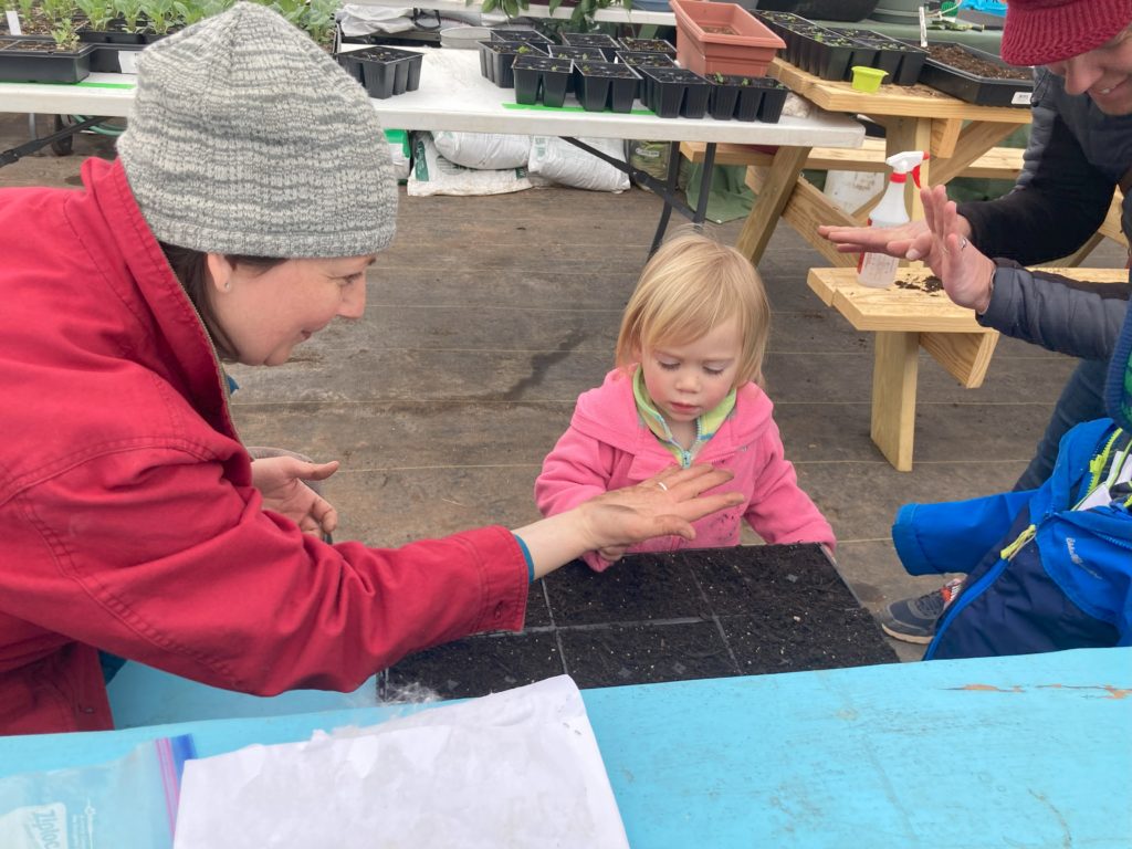 Woman holds a seed on her outstretched palm, showing two young children.