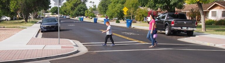 Two people cross a quiet street. The sidewalk juts into the street at the crosswalk in an almost "P" shape; this is a bump out.