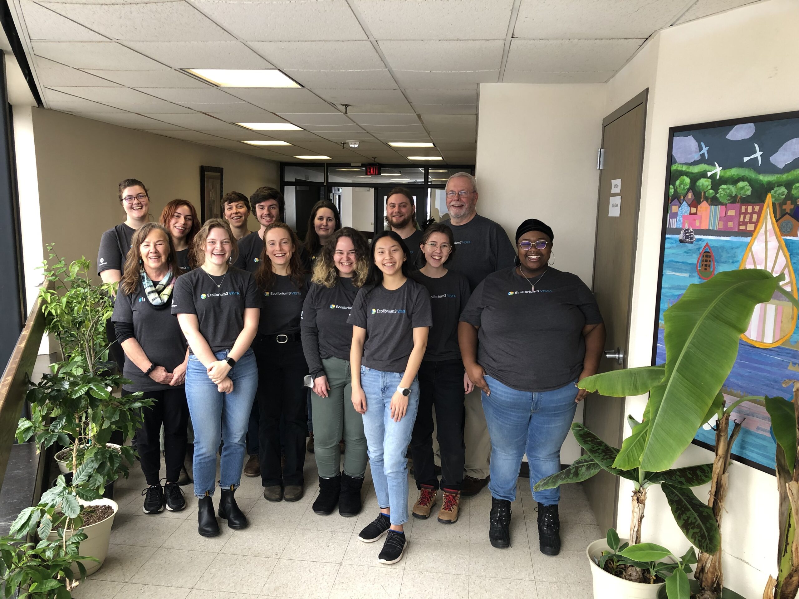 Group photo of VISTA members, smiling in matching tshirts in a hallway at the Eco3 office.