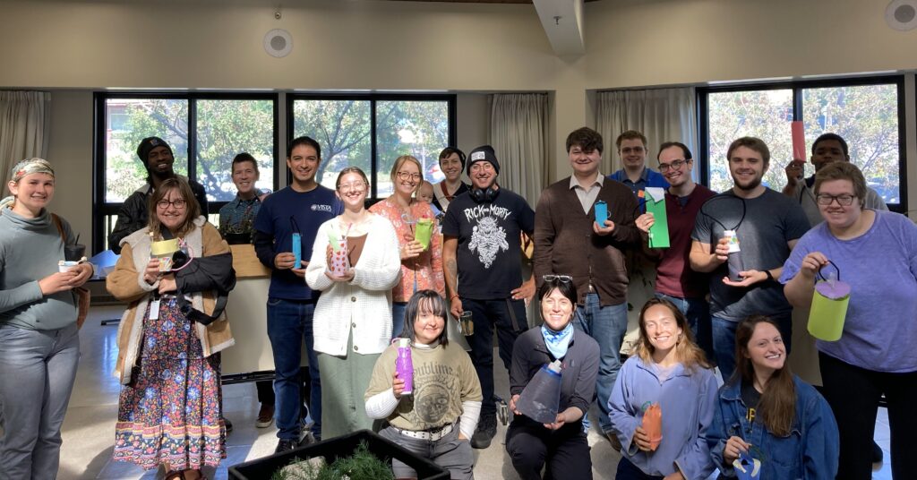 Group photo of VISTA members smiling and holding crafted water bottles after a team building design exercise.