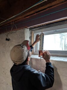 Person uses a caulk gun to seal around a basement window.