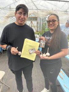 Two people smile while holding garlic, seed packets, and pages of instructions from garlic planting workshop.