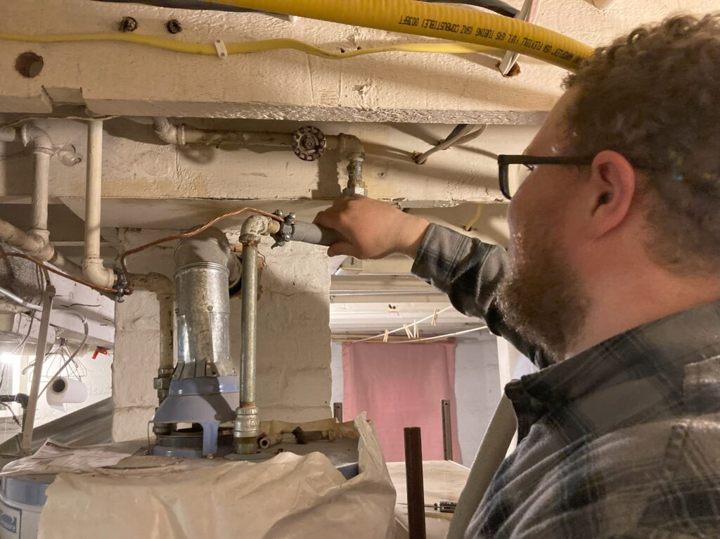 Energy auditor insulates a pipe leading into a hot water heater.