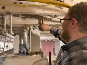Energy auditor insulates a pipe leading into a hot water heater.