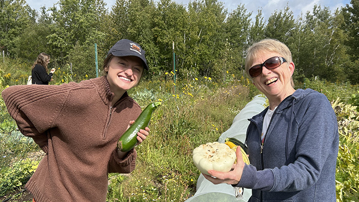 Two people smile over a large squash in the field at the Farm.