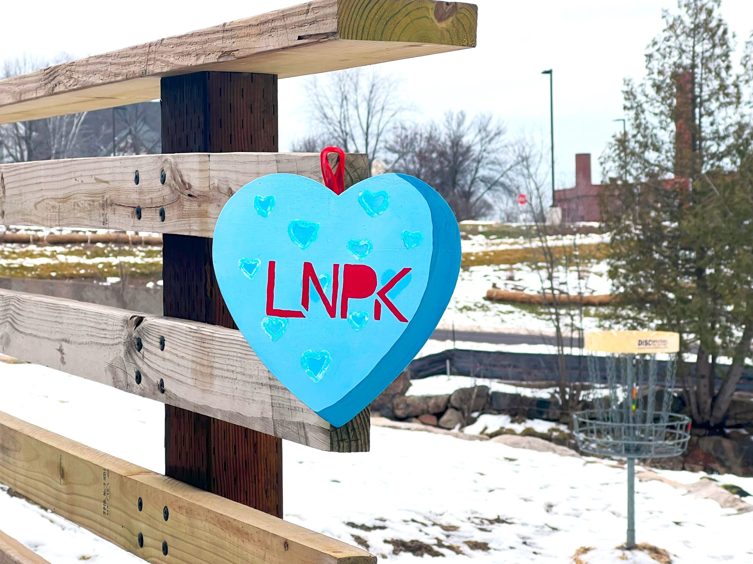 Blue heart with sparkly dots and "LNPK" in red hangs on a wooden bridge.