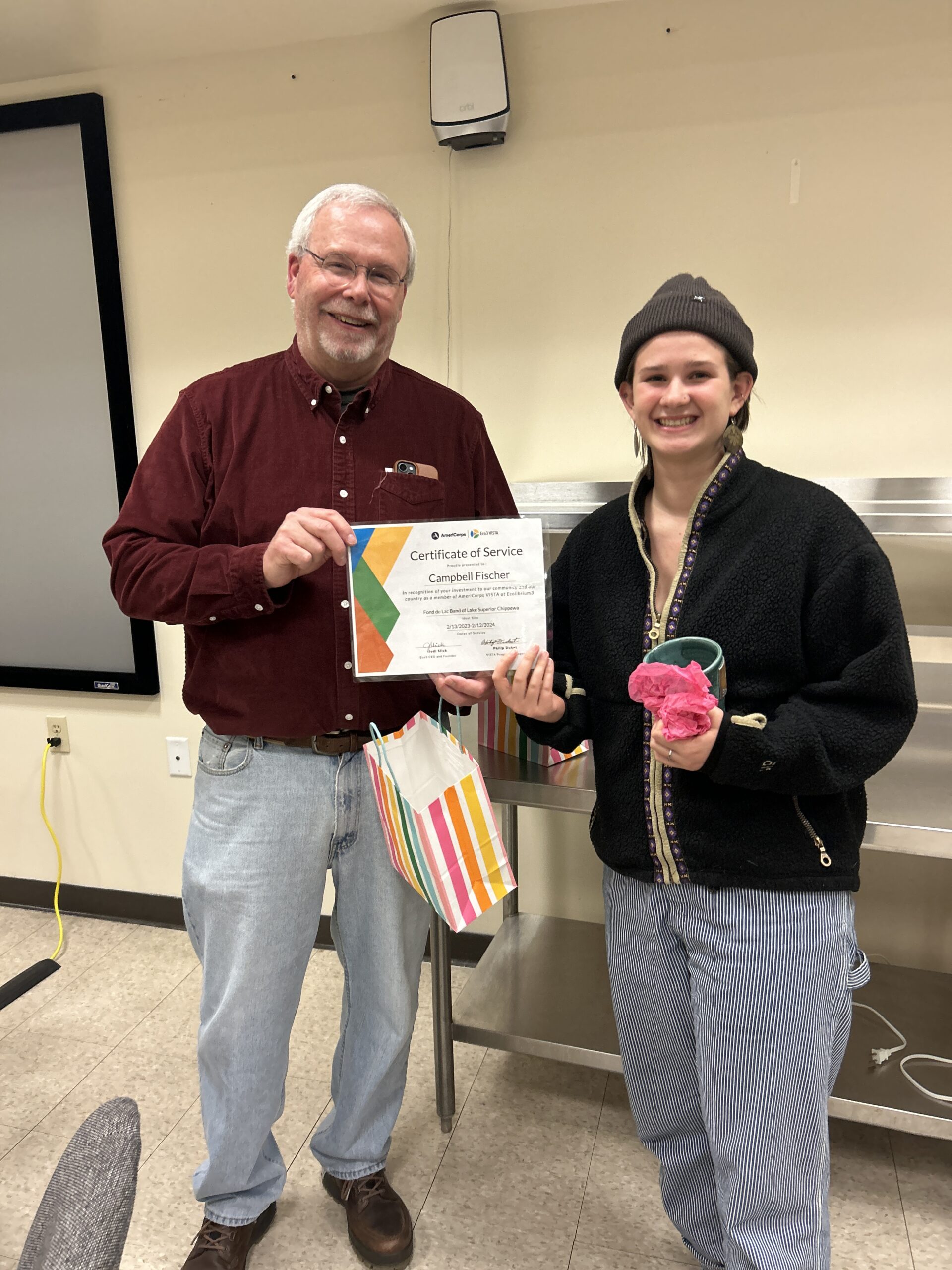 Two people smile at the camera while holding a colorful certificate between them.