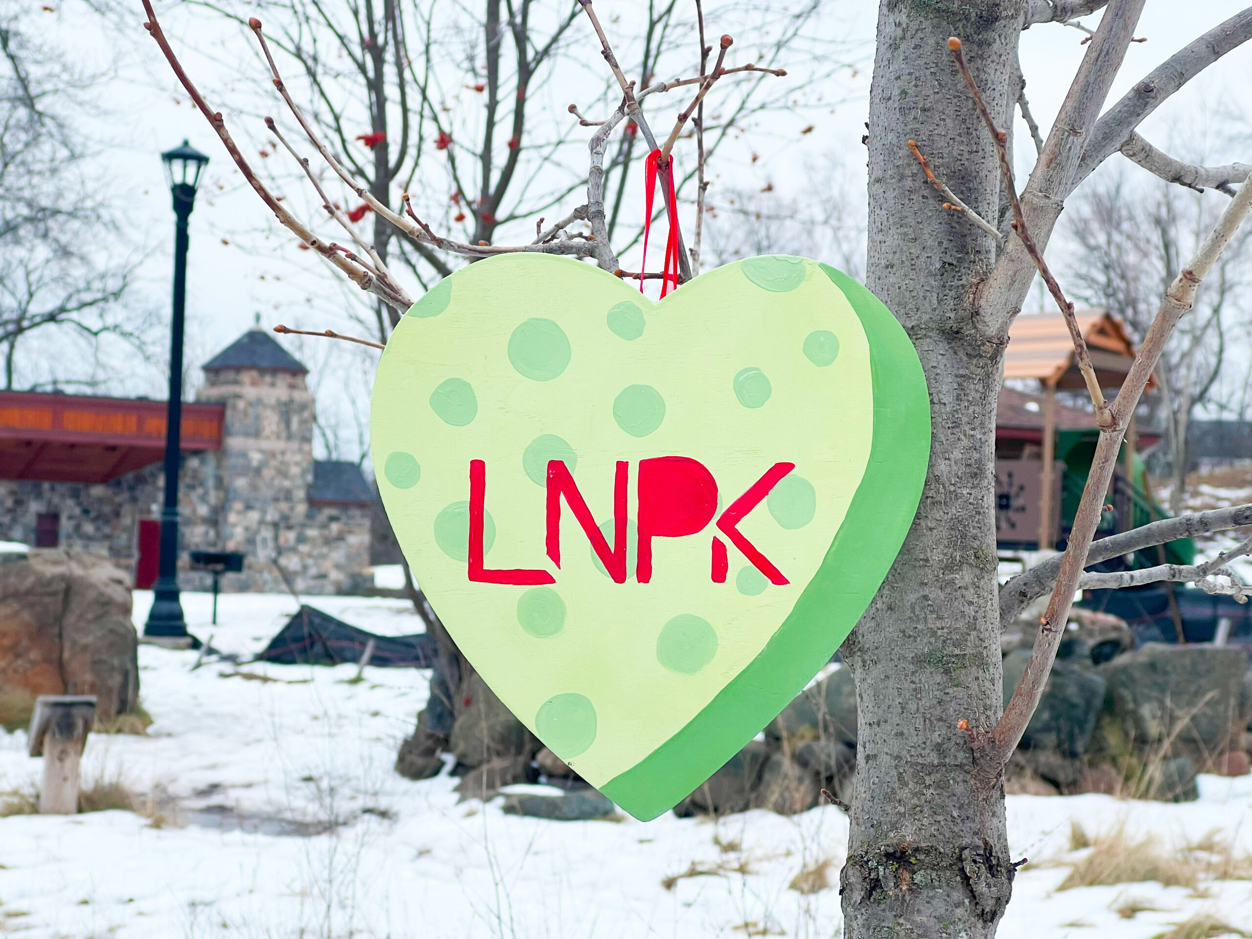 Light green heart with polka dots and "LNPK" in red hangs on a tree in front of the Lincoln Park pavilion.