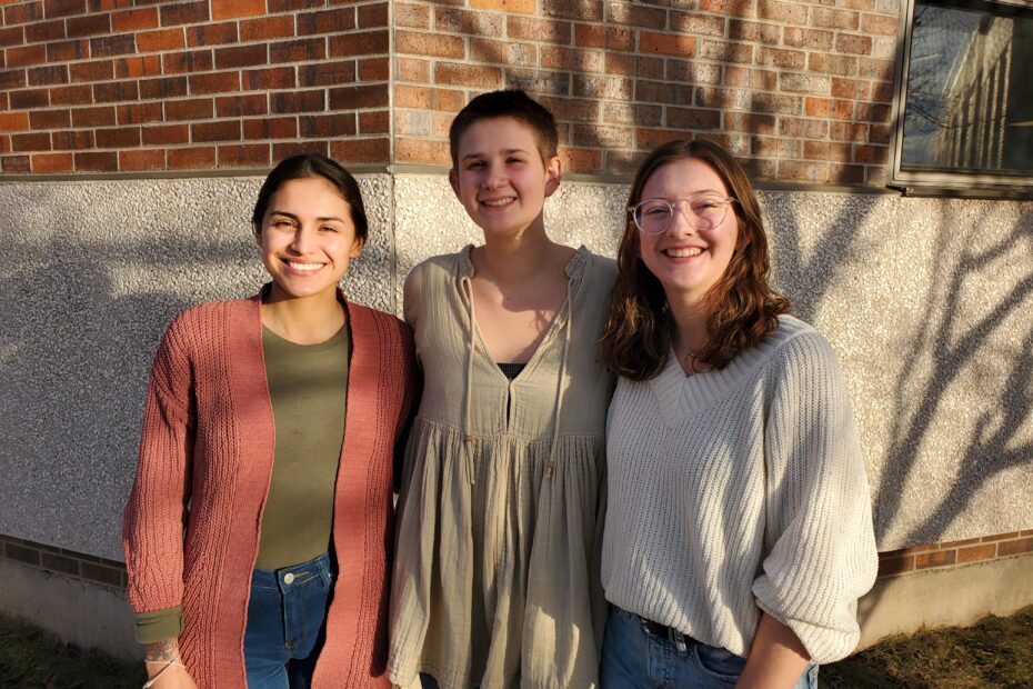 Three people smile at the camera in the afternoon sun.