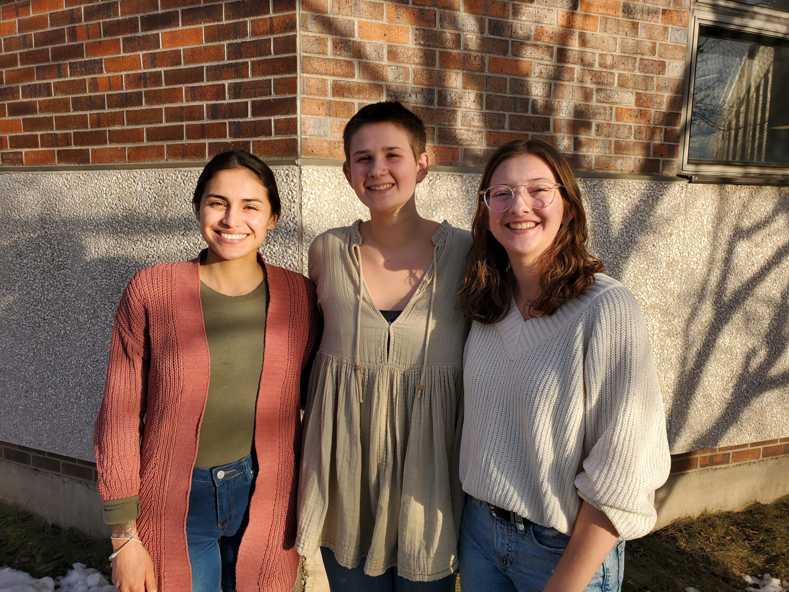 Three people smile at the camera in the afternoon sun.