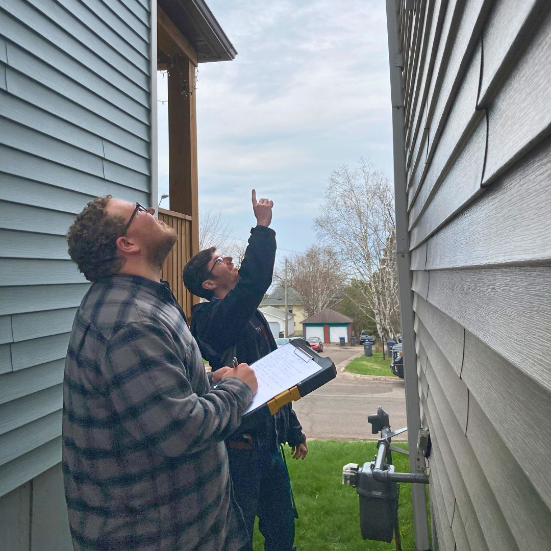 Two people point at the exterior of a house, looking up.