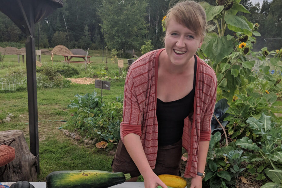 Person smiles at the camera while arranging vegetables on a table outside.