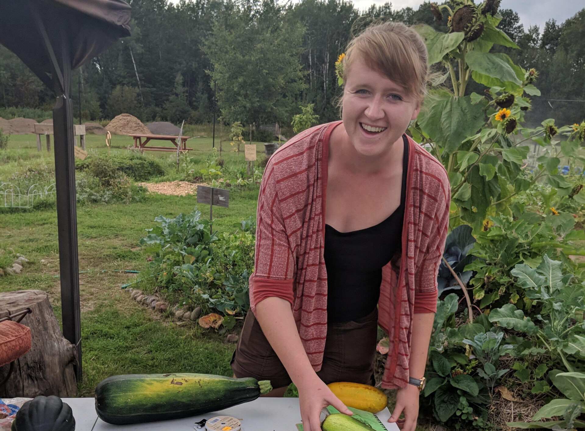 Person smiles at the camera while arranging vegetables on a table outside.